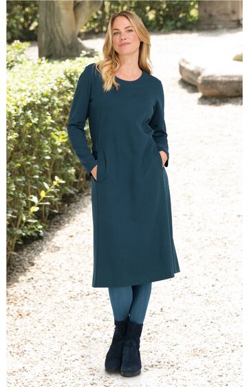 Dunkelgrünes Midikleid, lange Ärmel, Rundhalsausschnitt, seitliche Taschen, gerade geschnitten, getragen von stehender Frau mit verschränkten Armen