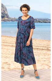 Knielanges Kleid in Dunkelblau mit roten und hellblauen Blumenmustern, halblange Ärmel, Rundhalsausschnitt, taillierte Form getragen von einer lächelnden Frau am Strand, mit hellblauen Sandalen