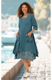 Blaugrünes Kleid, zweilagig mit ärmelloser, gemusteter Innenschicht und langer, unregelmäßiger, einfarbiger Außenschicht mit 3-4-Arm-Ärmeln, Rundhalsausschnitt, seitlichen Taschen, getragen von stehender Frau, knieumspielend