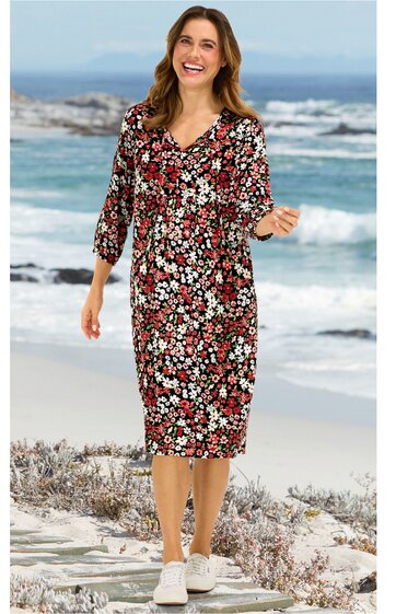 Knielanges, rot-schwarzes Kleid mit weißem Blumenmuster, V-Ausschnitt, 3/4-Ärmel, gerade geschnitten, getragen von lächelnder Frau am Strand, legerer Stil