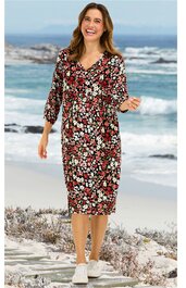 Knielanges, rot-schwarzes Kleid mit weißem Blumenmuster, V-Ausschnitt, 3/4-Ärmel, gerade geschnitten, getragen von lächelnder Frau am Strand, legerer Stil