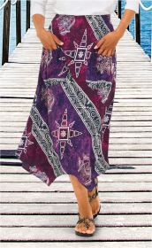 Viskose-Rock in Lila und Bordeaux mit weißem Ethno-Muster, asymmetrischem Saum und aufgesetzten Taschen, kombiniert mit weißem Oberteil und schwarzen Sandalen, stehend auf Holzsteg am Wasser