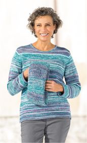 Frau mit lockigem grauem Haar lächelt, trägt gestreiften Baumwoll-Pullover in Blau- und Lilatönen und hält passenden, gefalteten Pullover vor dem Oberkörper, vor hellem Hintergrund