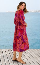 Frau in rotem und lila gemustertem Viskose-Kleid mit 3/4-Ärmeln und Gürtel, steht seitlich auf Holzsteg vor Meer, trägt braune Sandalen, Blick über die Schulter zum Betrachter, sommerlich, modisch, entspannt