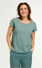 lächelnde Frau trägt ein mintgrünes Baumwoll-Shirt mit kurzem Arm, rundem Ausschnitt und strukturierter Oberfläche, kombiniert mit gemusterten, blauen Hosen, Hände in den Hosentaschen, vor hellem Hintergrund