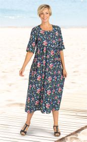 Frau am Strand trägt knielanges, blaues Viskose-Kleid mit buntem Blumenmuster, halblangen Ärmeln und Knopfleiste, dazu schwarze Sandalen mit Riemchen, lächelnd, stehender Pose auf Holzsteg vor Meer und Sandstrand