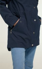 Detailansicht einer dunkelblauen Baumwoll-Jacke mit Metall-Druckknöpfen, zwei seitlichen Reißverschlusstaschen mit Händen darin, kombiniert mit hellblauen Jeans.