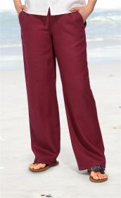 Bordeauxrote Leinen-Hose mit weitem Bein, getragen mit weißen Oberteil und braunen Sandalen am Strand, Hände in den Taschen.