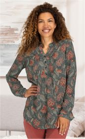 Frau mit lockigen braunen Haaren trägt eine grüne Modal-Bluse mit roten und beigen Blumenmustern, Knopfleiste und Stehkragen, kombiniert mit roten Hosen, steht lächelnd vor hellem Hintergrund, Hand in Hüfte gestützt.