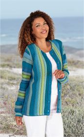 Frau trägt Baumwoll-Strickjacke mit senkrechten Streifen in Blau-, Grün- und Türkistönen, weiße Bluse und weiße Hose, steht lächelnd in natürlicher Landschaft mit Pflanzen und Meer im Hintergrund