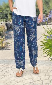 Beinaufnahme einer Person mit weißen Sandalen und einer dunkelblauen Viskose-Hose mit weiß-blauem Blumenmuster, kombiniert mit einem weißen Oberteil, stehend auf gepflastertem Weg mit Pflanzen im Hintergrund
