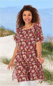 Frau am Strand trägt rot gemusterten Viskose-Kaftan mit Blumenmotiven, kurze Ärmel, seitliche Schlitze, weiße Hose, lockige Haare, lächelnd, blauer Himmel, Dünen und Gras im Hintergrund