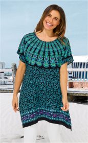 Frau am Strand trägt einen bunten Viskose-Kaftan mit blau-grünem Muster und weißer Hose, lächelt, hat schulterlange braune Haare, Hintergrund mit Strandkörben und Holzsteg unter blauem Himmel.