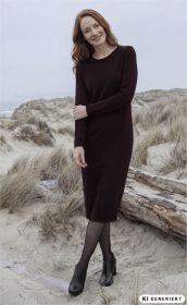 Frau mit roten Haaren trägt ein langärmliges, dunkelrotes Baumwoll-Mix-Kleid, schwarze Strumpfhose und schwarze Stiefeletten, steht lächelnd am sandigen Dünenstrand mit trockenem Gras und Treibholz im Hintergrund