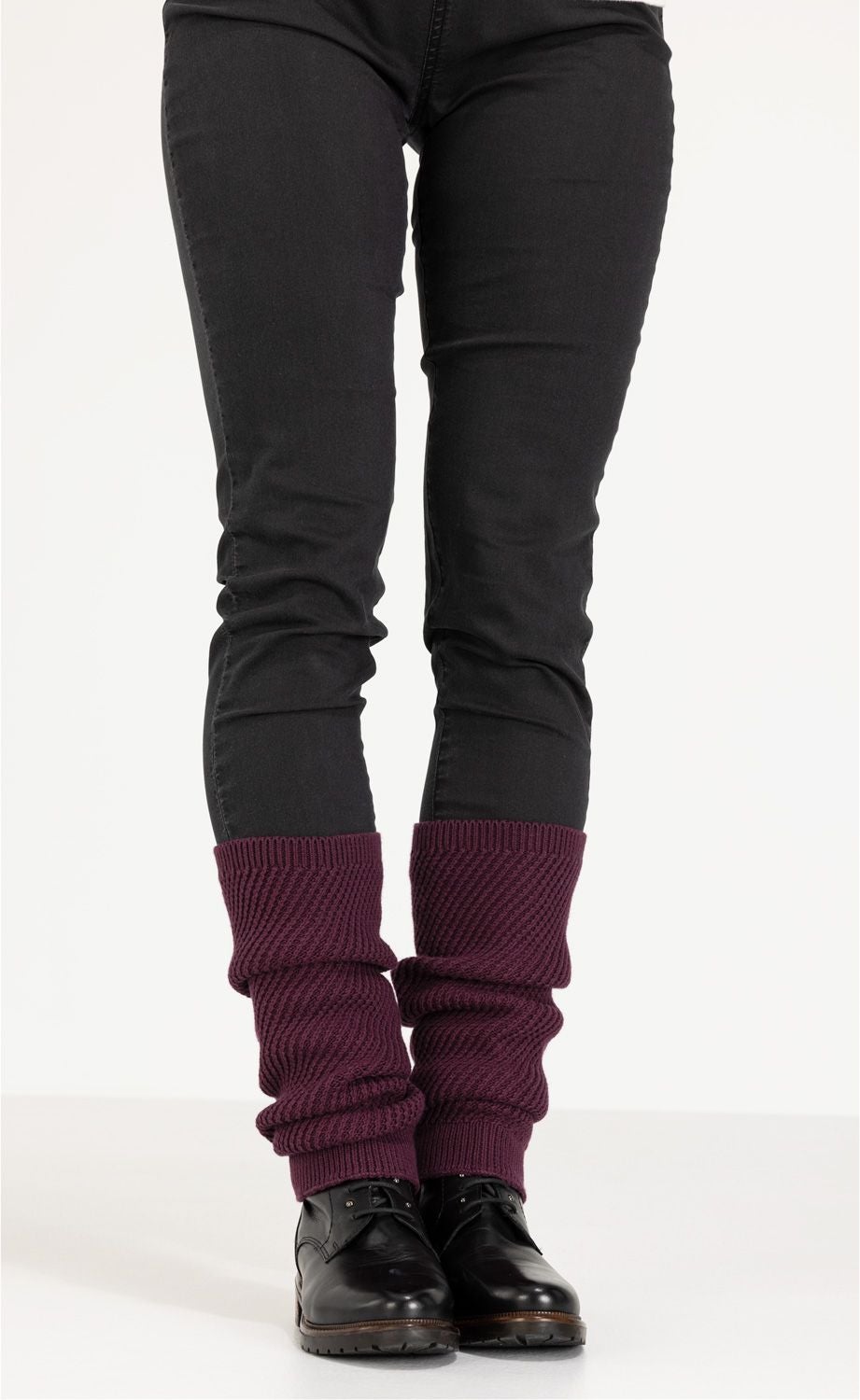 Beine in schwarzer Hose, schwarze Schnürschuhe, dunkelrote gestrickte Baumwoll-Mix-Stulpen, die lässig über den Schuhen getragen werden