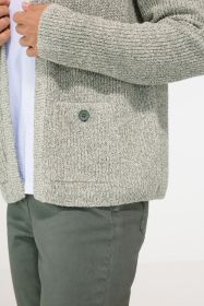 Detailansicht einer hellgrauen Baumwoll-Strickjacke mit grobem Rippstrickmuster, aufgesetzter Tasche mit Knopf, getragen über weißem Shirt, kombiniert mit dunkelgrüner Hose