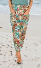 Person trägt bunte Viskose-Hose mit Patchwork-Muster in Türkis, Rot, Braun und Beige, Hände in Taschen, steht barfuß mit braunen Sandalen auf hellem Sandstrand