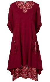 Bordeauxrotes Baumwoll-Kleid mit 3/4-Ärmeln, floral gemustertem Rundhalsausschnitt, zwei großen Taschen mit Knopf-Details vorne, asymmetrischem Saum und floral gemusterter Unterlage sichtbar am Saum und Ärmelumschlägen.
