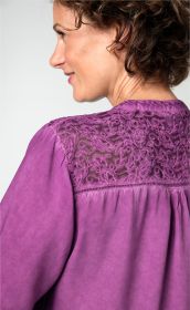 Frau von hinten mit kurzem lockigem Haar trägt lilafarbene Viskose-Bluse mit floraler, transparenter Spitzenstickerei am oberen Rücken und langen Ärmeln