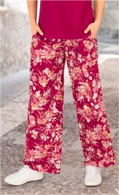 Beine in weiten Viskose-Hosen mit rosa und cremefarbenem Blumenmuster, kombiniert mit weißen Sneakern und einem dunkelroten Oberteil, stehend auf gepflastertem Boden