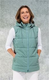 Frau mit schulterlangen braunen Haaren trägt eine mintgrüne, gesteppt Baumwoll-Weste mit Kapuze, Reißverschluss und Taschen, weißes 3/4-Arm-Shirt und weiße Hose vor grauer Wand, lächelt und hat Hände in den Taschen.