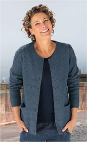 lächelnde Frau mit kurzen lockigen Haaren trägt dunkelblaue Strickjacke und dunkles Oberteil, steht outdoor an einer Steinbrücke mit verschwommenem Hintergrund