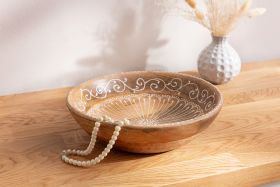 Runde Holz-Schale mit filigrarem weißem Muster innen, liegt auf hellem Holztisch, mit Perlencollier am Rand, im Hintergrund weiße Vase mit Trockenblumen vor heller Wand