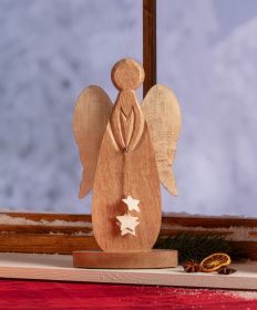 Holz-Engel mit geschnitztem Körper und Flügeln, hält an einer Schnur drei weiße Sterne, steht auf einem Holzsockel vor Fenster mit verschneitem Hintergrund, dekoriert mit getrockneter Orangenscheibe und Sternanis auf rotem Tuch.