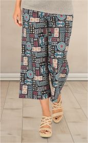 Baumwoll-Hose mit bunter Ethno-Musterung in Blau, Rot, Beige und Schwarz, weit geschnitten bis zur Wade, getragen mit beigefarbenen Sandaletten mit gekreuzten Riemen auf hellem Holzboden