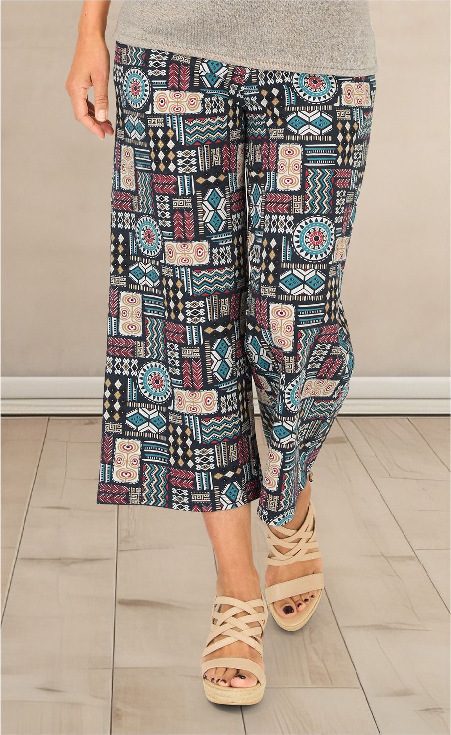Baumwoll-Hose mit bunter Ethno-Musterung in Blau, Rot, Beige und Schwarz, weit geschnitten bis zur Wade, getragen mit beigefarbenen Sandaletten mit gekreuzten Riemen auf hellem Holzboden