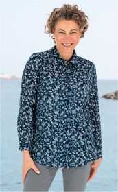 Frau mit lockigen kurzen Haaren trägt dunkelblaue Viskose-Mix-Bluse mit hellblauem Blattmuster, steht lächelnd am Wasser, hellgraue Hose sichtbar, entspannte Pose