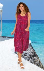 Frau in ärmellosem, rosarot gemustertem Viskose-Kleid mit Blumenmuster, weiße Sandalen, steht am weißen Strand mit blauem Meer und klarem Himmel im Hintergrund.