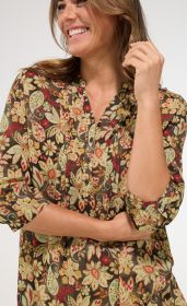 Frau trägt bunte Modal-Bluse mit floralem Muster in Rot-, Grün- und Beigetönen, halblange Ärmel mit Knopf, Stehkragen, Knopfleiste vorne, lächelnd, rechte Hand am Kopf, linker Arm vor dem Körper verschränkt
