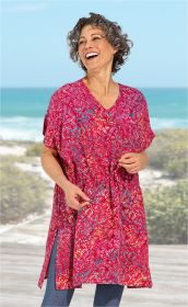 Frau am Strand trägt roten Viskose-Kaftan mit floralem Muster, V-Ausschnitt und Tunnelzug in der Taille, lacht, kurze lockige Haare, dahinter Meer und bewachsene Dünen, leichte Sommerstimmung