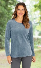 lächelnde Frau mit langen braunen Haaren, trägt hellblaues langärmeliges Shirt und dunkle Hose, unscharfer grüner Hintergrund mit Bäumen und Lichtpunkten