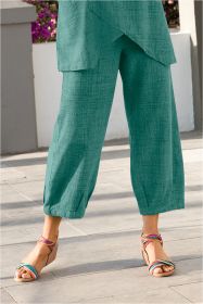 Hose aus grüner Baumwolle mit lockerem, weitem Schnitt und gekräuseltem Saum, kombiniert mit bunten, mehrfarbigen Sandalen mit Keilabsatz, auf grauem Steinboden stehend.