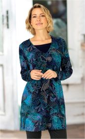 Frau mit kurzen blonden Haaren trägt langärmeliges Baumwoll-Mix-Shirt mit blau-grünem abstraktem Punkte- und Musterdesign, V-Ausschnitt, steht vor hellem Hintergrund, Hände locker vor dem Bauch verschränkt.