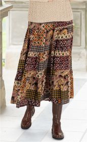 Viskose-Rock mit buntem Patchwork-Muster in Rot-, Gelb- und Schwarztönen, kombiniert mit braunen Lederstiefeln und beige-grauem Grobstrickpullover, aufgenommen auf hell gebfließtetem Boden vor hellem Hintergrund