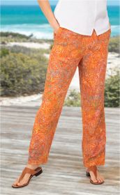 Frau trägt orange Viskose-Hose mit buntem, geschwungenem Muster, weißes Oberteil, braune Sandalen, steht auf Holzsteg mit Meer und Vegetation im Hintergrund.