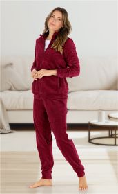 Frau barfuß in rotem Velours-Jogginganzug mit Reißverschlussjacke und Hose stehend in modernem Wohnzimmer vor weißem Sofa und rundem Beistelltisch