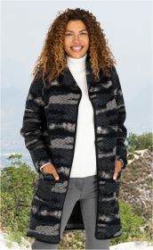 Frau trägt Woll-Mix-Mantel mit dunklem Muster, weißem Rollkragenpullover und grauer Hose vor Berglandschaft, Hände in Manteltaschen, lockige Haare, lächelnd