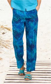 Blaue Viskose-Hose mit abstraktem Muster in verschiedenen Blautönen, weit geschnitten, getragen mit türkisfarbenen Sandalen, Strandhintergrund, Hände in den Hosentaschen, türkisfarbenes Oberteil teilweise sichtbar