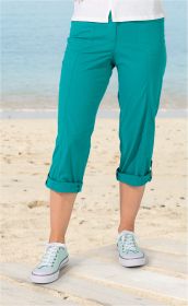Frau trägt türkisfarbene Baumwoll-Mix-Hose in Capri-Länge mit aufgekrempelten Beinen und weiße Sneakers am Sandstrand vor blauem Meereshintergrund