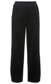 Schwarze Baumwoll-Hose mit Elastikbund, geradem Schnitt und zwei seitlichen Eingrifftaschen, aus weich geripptem Cordstoff, ohne sichtbaren Verschluss.