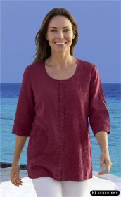 Frau trägt rote Baumwoll-Bluse mit Knopfleiste und filigranen Stickereien, 3/4-Ärmel, steht vor blauem Meer und Himmel, blickt lächelnd in die Kamera
