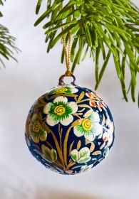 Hängende Kugel mit blauem Grund, verziert mit goldfarbenen Zweigen und weißen Blumen mit gelben und grünen Details, an grünen Tannenzweigen befestigt