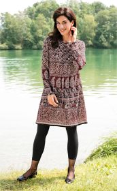 Frau steht am Seeufer, trägt langärmeliges Viskose-Kleid mit braunem und beigem Ornamentmuster, schwarze Leggings und schwarze Ballerinas, lächelnd, dunkle mittellange Haare, grüne Bäume im Hintergrund, sonniger Tag