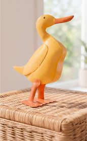 gelbe Deko-Ente aus Holz mit orangem Schnabel und Beinen stehend auf einem geflochtenen Korb, hintergrund unscharf mit hellem Fensterlicht