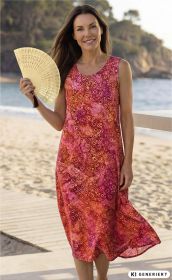 Frau am Strand trägt rotes Viskose-Kleid mit gelb-rosa Spiralmuster, hält dekorativen Fächer, lächelnd, braune Haare, sonnige Strandkulisse mit Sand, Meer und Felsen im Hintergrund.