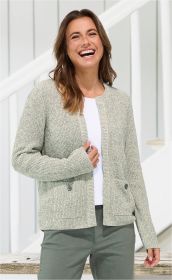 Frau trägt hellgraue Baumwoll-Strickjacke mit Knöpfen und Taschen, weißes Shirt und grüne Hose, lächelt, steht vor weißem Treppengeländer im hellen Raum